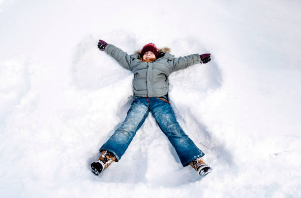 Small red haired girl making snow angle. Calm winter snowy day in a beautiful forest during daytime. Smiling red haired girl making snow angle. snow angels stock pictures, royalty-free photos & images