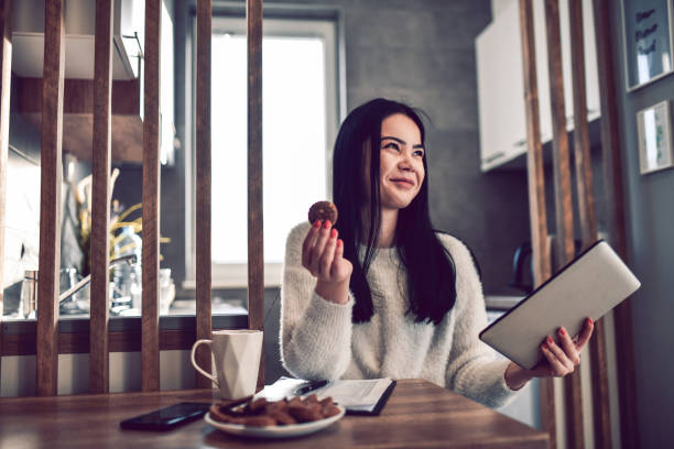 Smiling Female Eating Breakfast And Organizing Day With Clipboard And Digital Tablet