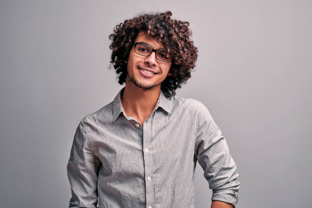 Waist up portrait of handsome eastern guy in gray shirt wearing eyeglasses on isolated gray background. Waist up portrait of handsome eastern guy in gray shirt wearind eyeglasses on isolated gray background. Arabian man with exotic curly hairstyle north african ethnicity stock pictures, royalty-free photos & images