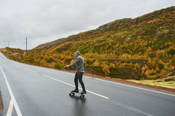 istock Young man riding a longboard on empty winding mountain road in summer, rear view. 1210217096