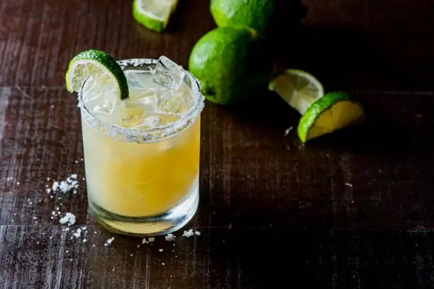 Photo of Margarita. Classic traditional Mexican cocktail. Made with Blanco tequila, fresh lime juice, agave syrup and orange juice. Served in salt rimmed tumbler over ice and garnished with a lime.