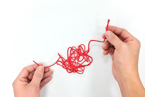 Hands fixing a tangled yarn in white background. Problem solving concept and critical thinling skills. Top view.