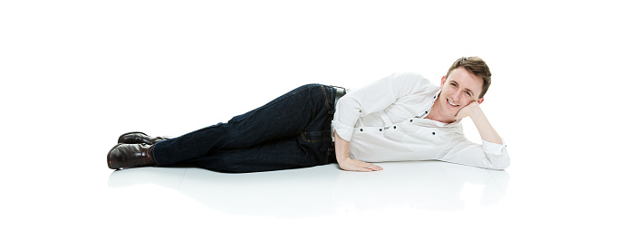 Side view of aged 20-29 years old with short hair caucasian young male lying down in front of white background wearing button down shirt who is cheerful