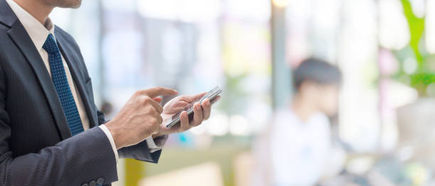 istock Businessman using smartphone online in blur office space banner background with copy space.Concept of people using technology. 1210249531