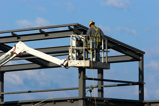 Construction worker on a cherry picker crane up at the roof of a high building