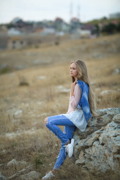 istock Female outdoors sitting on a big stone in jeans clothes 1210253204