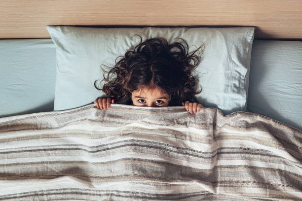 little girl covering her face with the bedspread - sleeping child bedtime little girls imagens e fotografias de stock