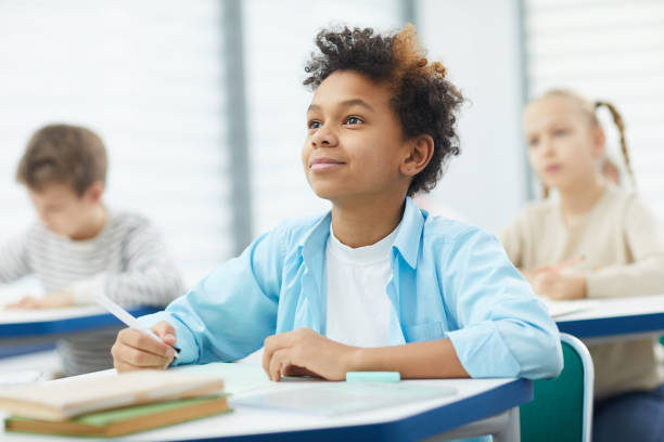 Attentive Black Boy In Class Horizontal potrait of young African American boy sitting at school desk attentively listening to his teacher, copy space schoolboy stock pictures, royalty-free photos & images