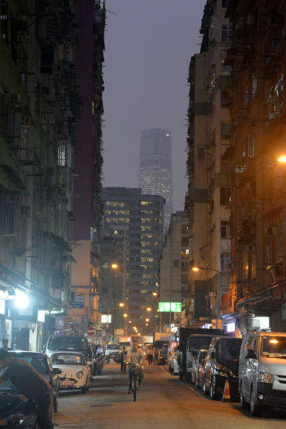 Tai Kok Tsui at dusk, Kowloon peninsula, Hong Kong Man cycling on the street in Tai Kok Tsui at dusk, an area west of Mong Kok in Kowloon, Hong Kong. In the distance, the International Commerce Centre skyscraper, the tallest building in Hong Kong at 484 mt. international commerce center stock pictures, royalty-free photos & images