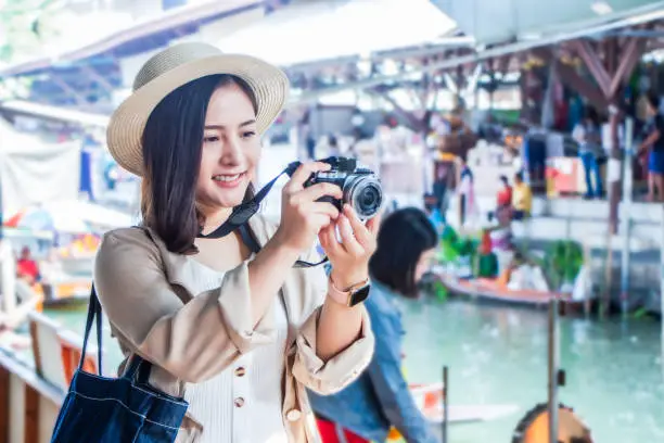 Photo of asia female tourists wearing hat holding camera and smartphone take photo vlog live . Beautiful woman visiting Damnoen Saduak floating market,Ratchaburi.