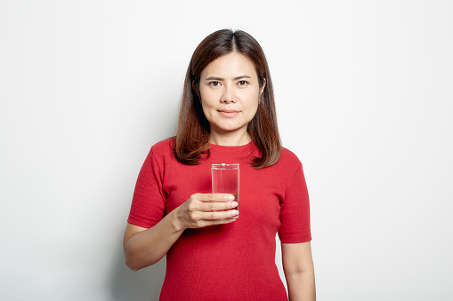 Attractive pretty asian woman in a red dress holding water glass on light gray banner background, Pure water concept and health care