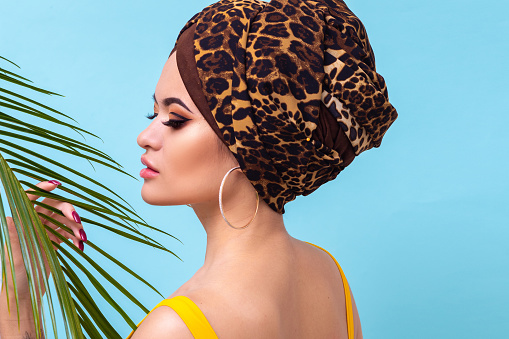 Summer sea and the hot weather, the beach trend. Young beautiful multi-ethnic woman in leopard turban and yellow swimsuit, blue background