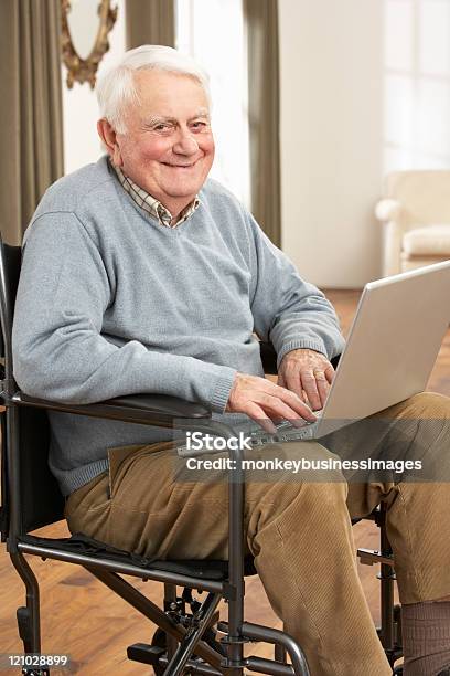 Disabile Uomo Anziano Seduto In Una Sedia A Rotelle Con Un Computer Portatile - Fotografie stock e altre immagini di 70-79 anni