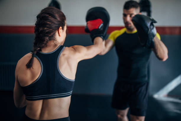 Young woman on kick box practice, learning from her coach while sparring with him Young woman on kick box practice, learning from her coach boxing technique while sparring with him self defense stock pictures, royalty-free photos & images