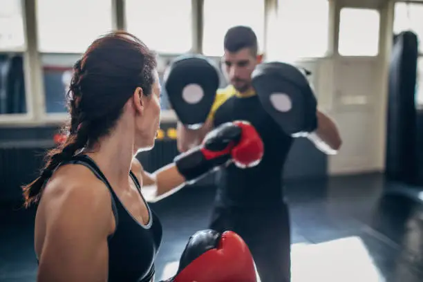 Young woman on kick box practice, learning from her coach boxing technique while sparring with him