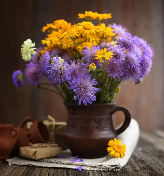 Bouquet of wildflowers (Anthemis tinctoria and Knautia arvensis) in a ceramic jug on the table