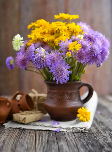 Bouquet of wildflowers (Anthemis tinctoria and Knautia arvensis) in a ceramic jug on the table