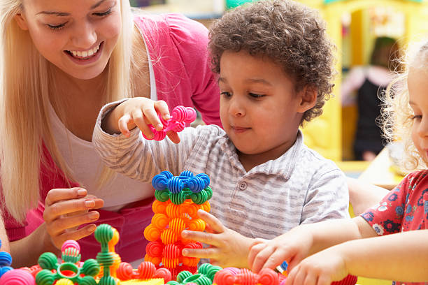 Young woman playing with boy in nursery school stock photo