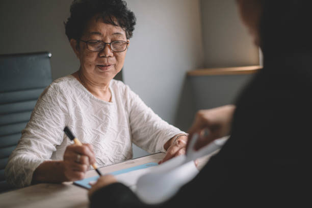 法的文書に署名する彼女の退職投資計画について彼女の中国のエージェントと話し合っているアジアの中国のアクティブな先輩女性 - senior adult women adult tan ストックフォトと画像