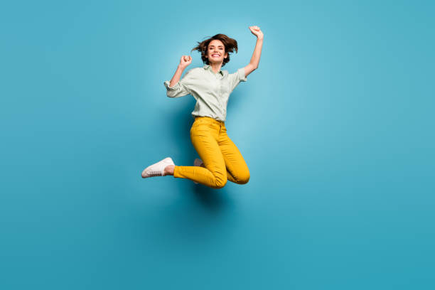 volledige lichaamsfoto van funky mooie dame die hoog omhoog springt die weekendvakantiestart viert draagt toevallige groene overhemd gele broekssneakers geïsoleerde blauwe kleurenachtergrond - springen stockfoto's en -beelden