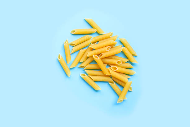 Uncooked penne pasta isolated on blue background.