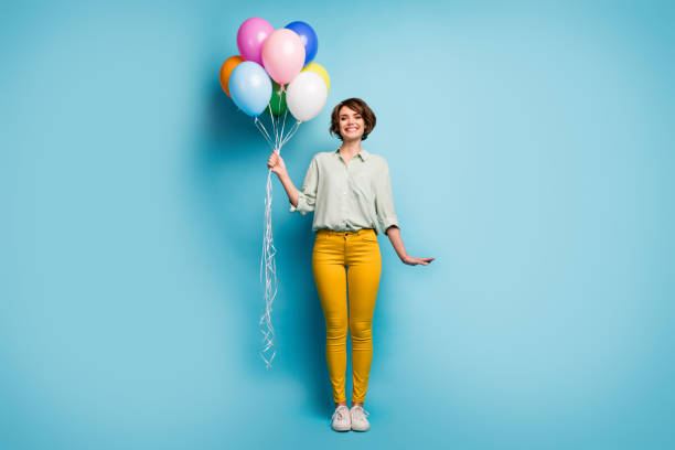 full längd foto av ganska söt bedårande lady överraskning födelsedagsfest hålla många färgglada luftballonger bära casual grön skjorta gula byxor skor isolerade blå färg bakgrund - kvinna ballonger bildbanksfoton och bilder