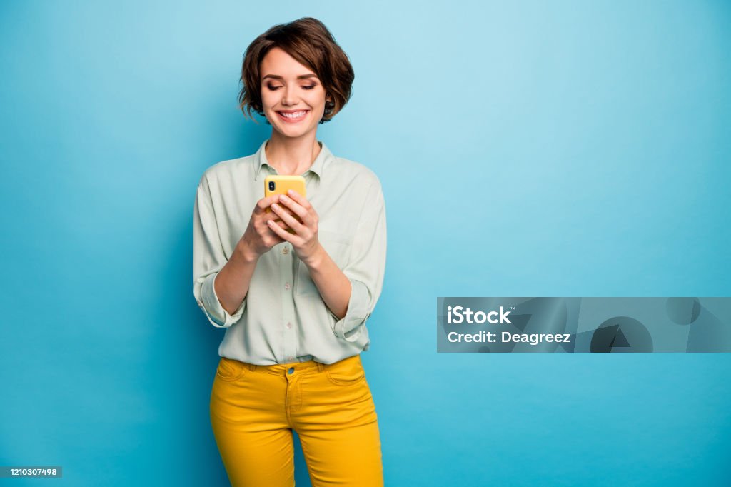 Photo of attractive lady holding telephone hands reading new blog post positive comments popular blogger wear casual green shirt yellow trousers isolated blue color background Photo of attractive lady holding telephone hands reading new blog post positive, comments popular blogger wear casual green shirt yellow trousers isolated blue color background One Woman Only Stock Photo