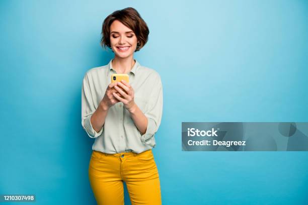 Photo Of Attractive Lady Holding Telephone Hands Reading New Blog Post Positive Comments Popular Blogger Wear Casual Green Shirt Yellow Trousers Isolated Blue Color Background Stock Photo - Download Image Now