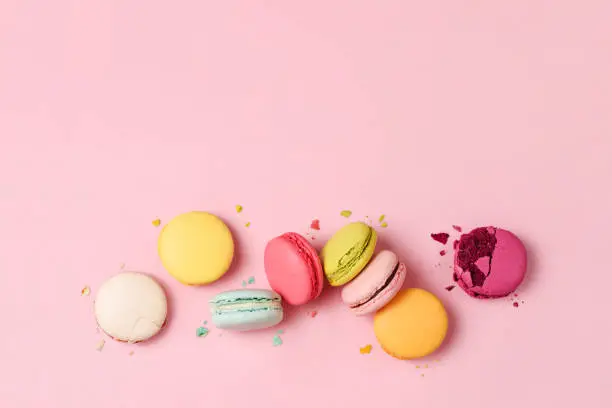 Photo of Mixed of colorful macaroni or pasta cake on a pink background. Sweet and colorful french macarons, pastel colors. Flat lay, top view. Add your text.