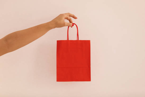 istock Red paper bag in woman's hand against pink background 1210316110