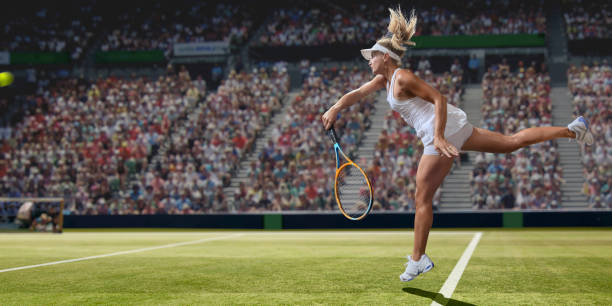 Professional Female Tennis Player Serving On Grass Court During Match A close up image of a professional female tennis player dressed in tennis whites and visor, in mid-air near baseline, having just played a serve. The athlete is playing on a grass court in a generic tennis stadium full of spectators on a sunny day. Selective focus on the player. game swing stock pictures, royalty-free photos & images