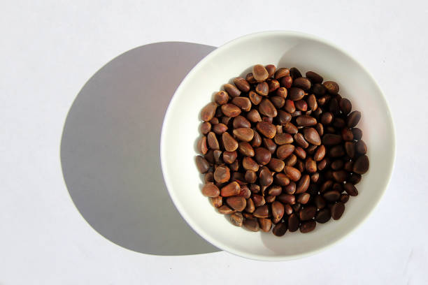 Unpeeled cedar pine nuts in white plate on white background
