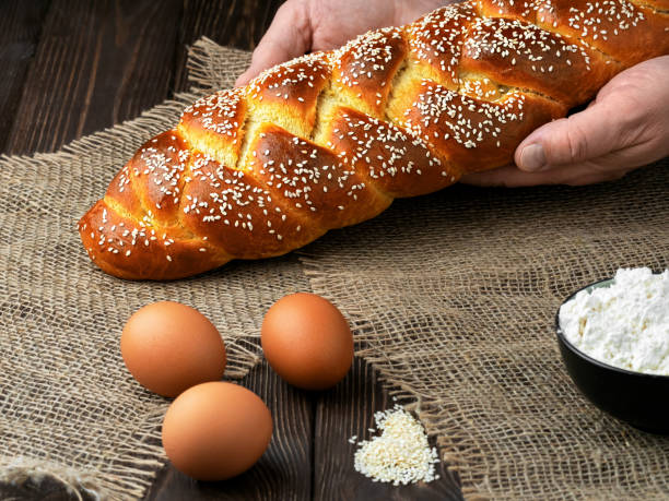 bäcker legt osterbrot auf den tisch. dunkle s-leinen hintergrund. nahaufnahme, flache schärfentiefe. zutaten zum kochen von geflochtenem brot. - hanukkah loaf of bread food bread stock-fotos und bilder