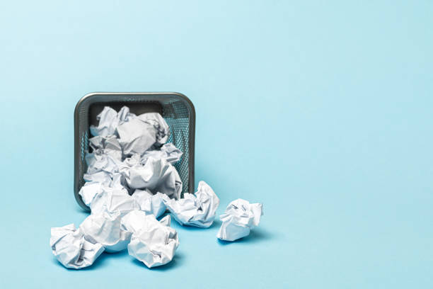 istock Overturned trash can with crumpled paper balls on a blue background 1210324631