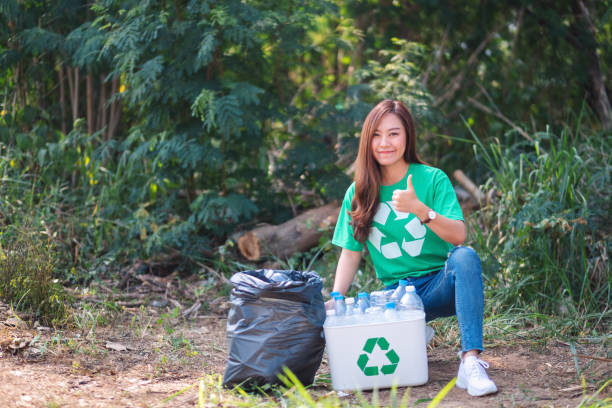 istock woman making thumbs up hand sign while collecting garbage plastic bottles into a recycle bin in the outdoors 1210331567
