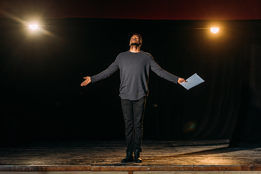 african american actor holding scenario and standing on stage during rehearse