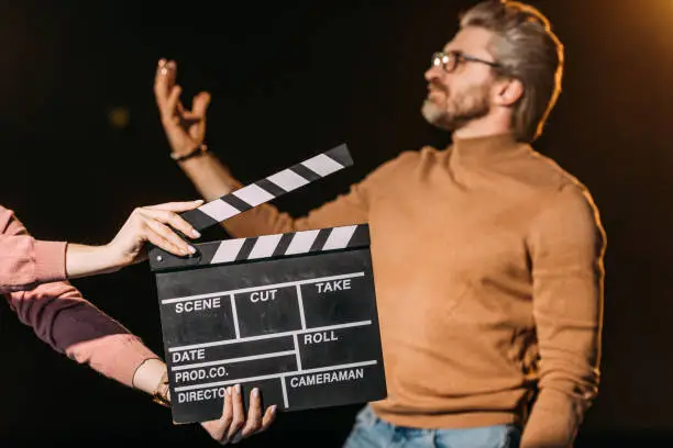 Photo of selective focus of mature actor performing role with clapboard in front