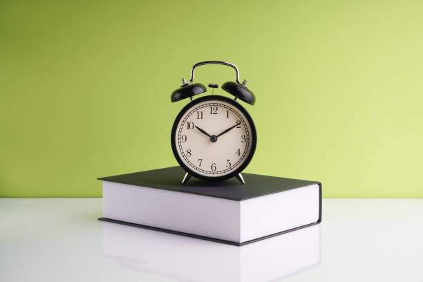 istock Alarm Clock and book on green background. 1210334491