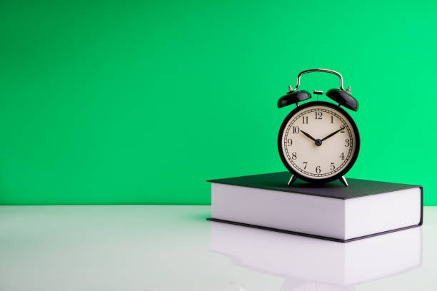 istock Alarm Clock and book on green background. 1210334494