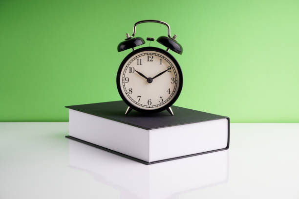 istock Alarm Clock and book on green background. 1210334526