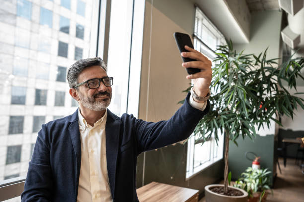 Mature businessman taking a selfie at office Mature businessman taking a selfie at office following moving activity photos stock pictures, royalty-free photos & images