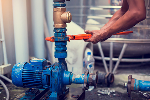 Plumber using a wrench to repair and remove the water supply pipe and valve. Plumbers working using orange pipe wrenches with blurry motor pump motor.