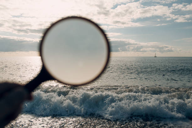 istock Man holds a magnifier and looks at the seascape 1210337987