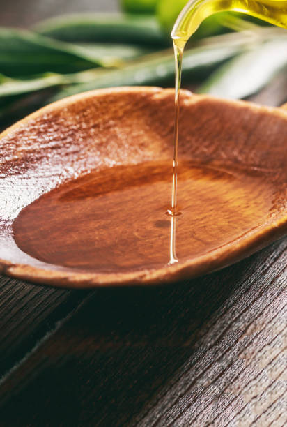 Olive oil in a wooden bowl on a table, closeup view Olive oil tasting. Pouring olive oil on a wooden spoon, closeup verical view. Extra virgin healthy olive oil drops olive oil pouring antioxidant liquid stock pictures, royalty-free photos & images