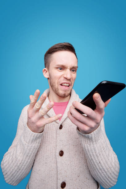istock Annoyed young man with furious expression looking at smartphone screen 1210340140