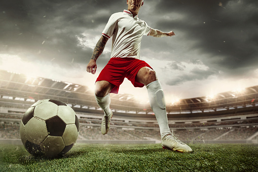 Football or soccer player at stadium in flashlight. Young male sportive model training, practicing. Moment of attacking, catching. Concept of sport, competition, winning, action, motion, overcoming.