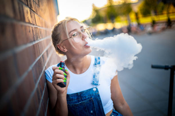 garota moderna ao ar livre fumando vaping cigarro eletrônico fazendo grande nuvem de fumaça - quit scene - fotografias e filmes do acervo