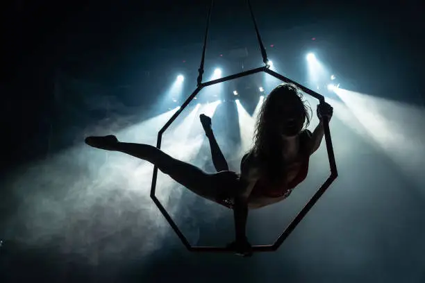 Photo of Silhouette of female Aerial acrobat on circus stage with spot lights on background