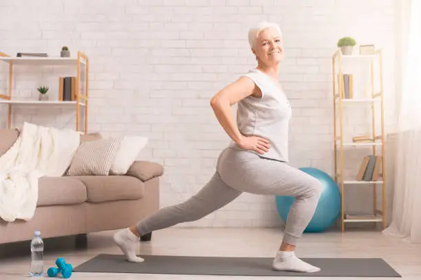 Legs stretching. Sporty senior lady doing lunges at home, empty space