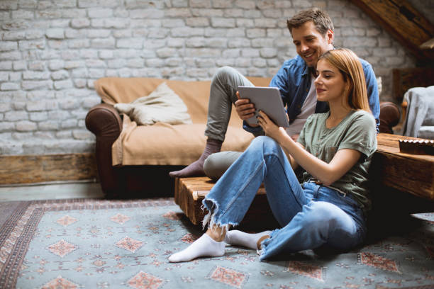 istock Happy couple using digital tablet while sitting  together oh the floor 1210350190
